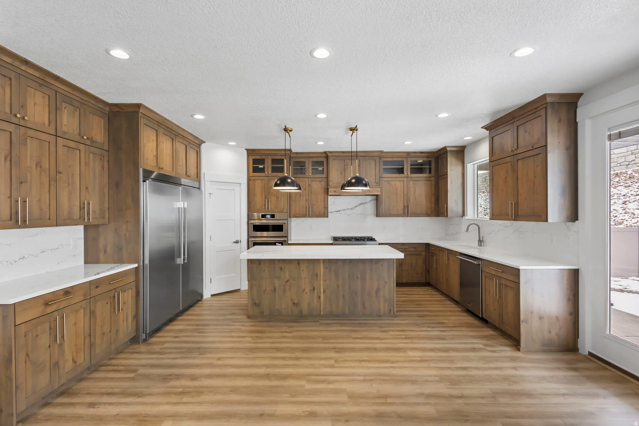 Spacious kitchen featuring extensive wood cabinetry, white countertops, a central island, recessed lighting, and stainless steel appliances