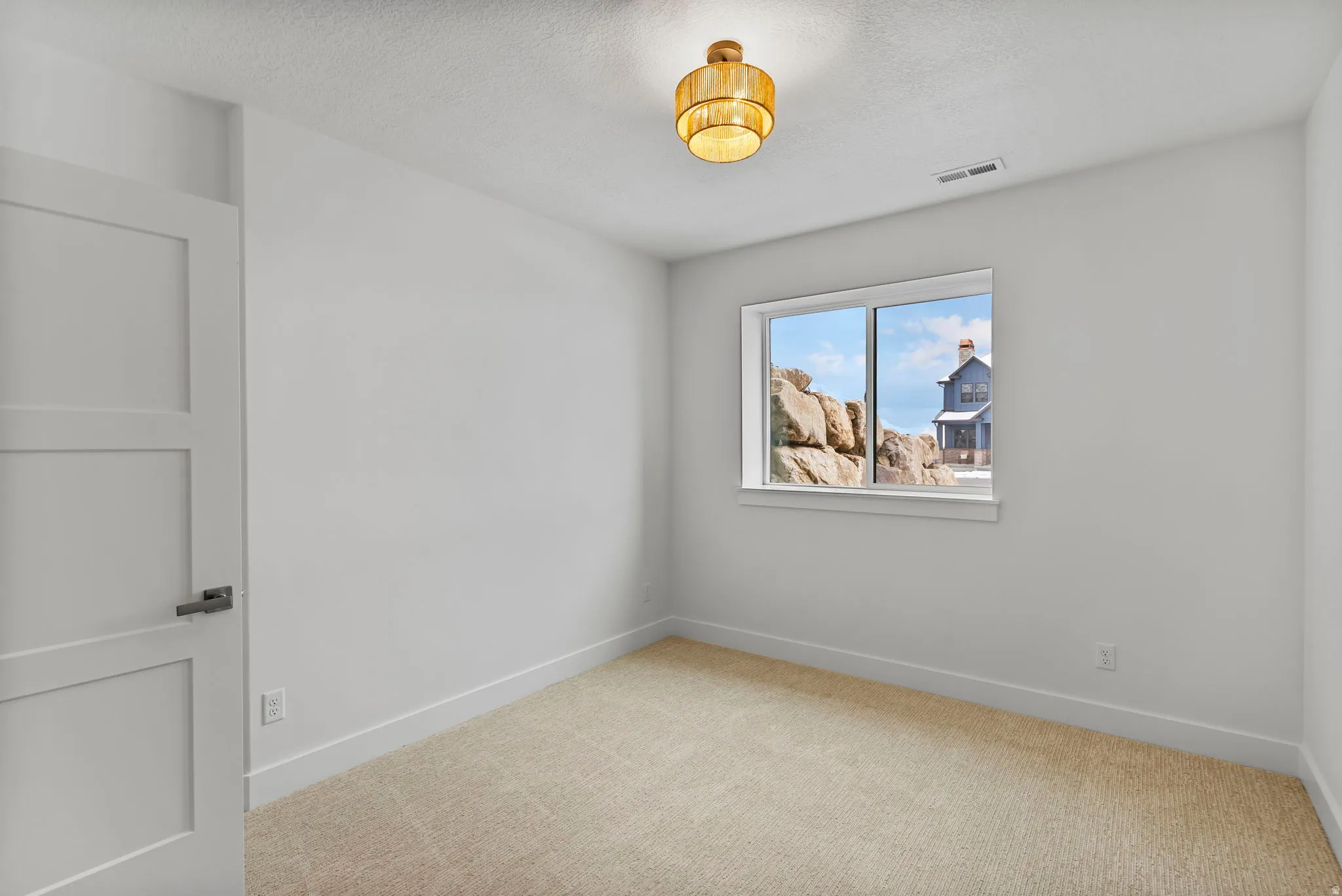 Neutral interior room featuring a light-colored carpet, white walls, and a contemporary light fixture