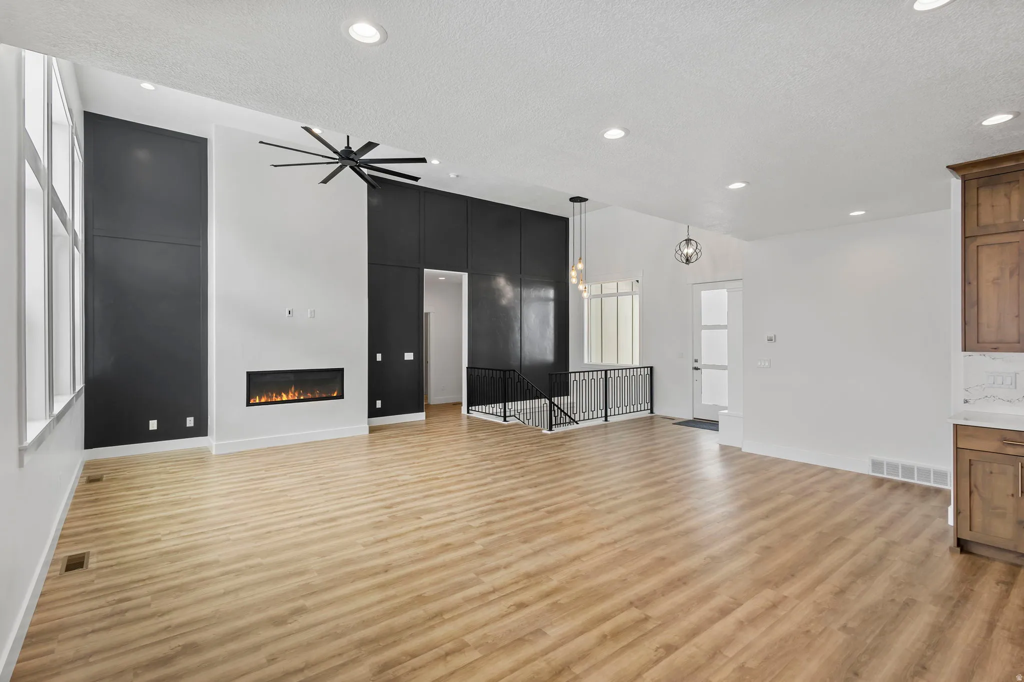 Vaulted ceiling great room featuring a linear electric fireplace, wood-finish flooring, a contemporary ceiling fan, and tall windows