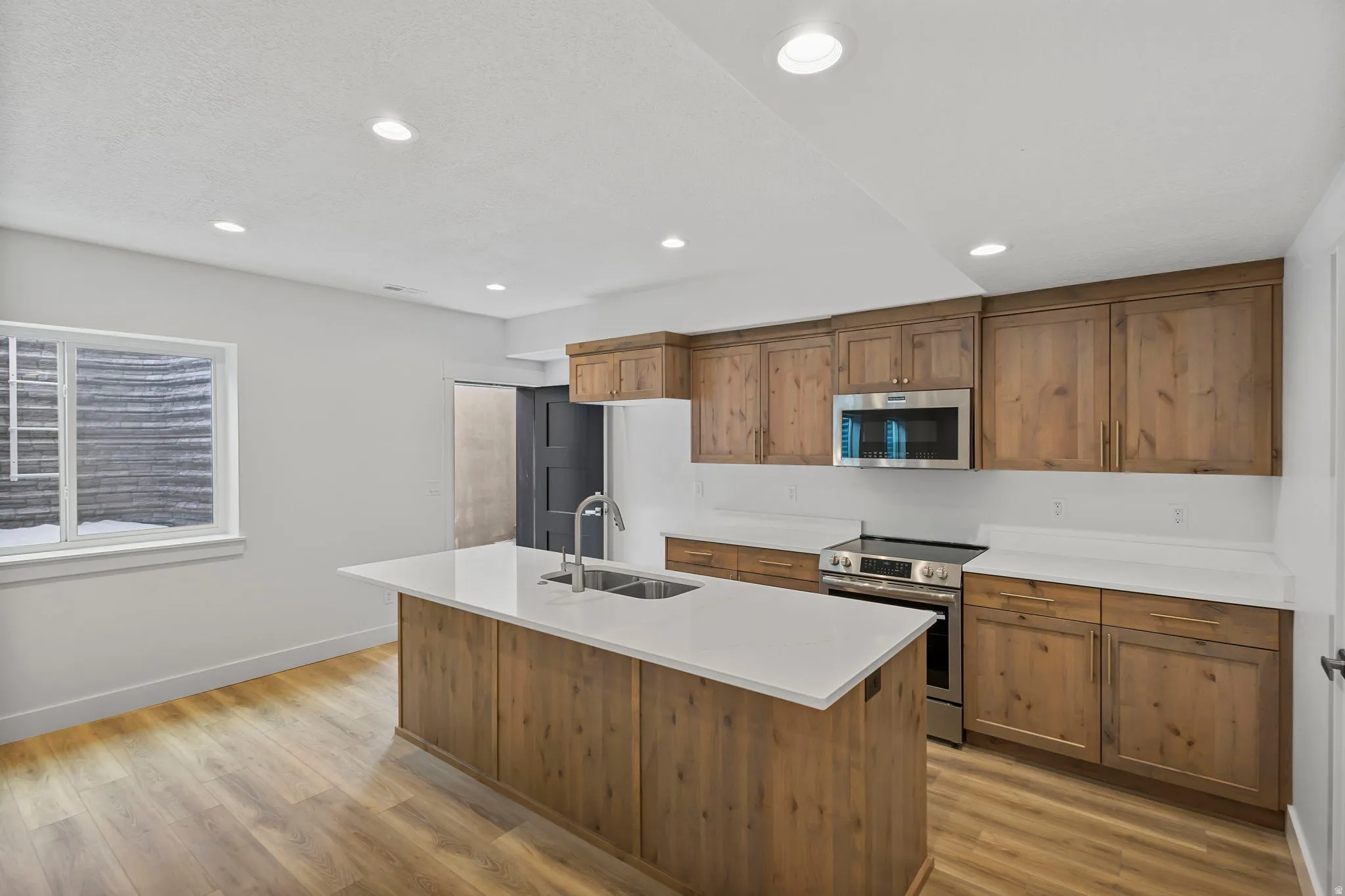 Bright kitchen featuring a central island with an undermount sink, light countertops, wood-finish flooring, and recessed lighting