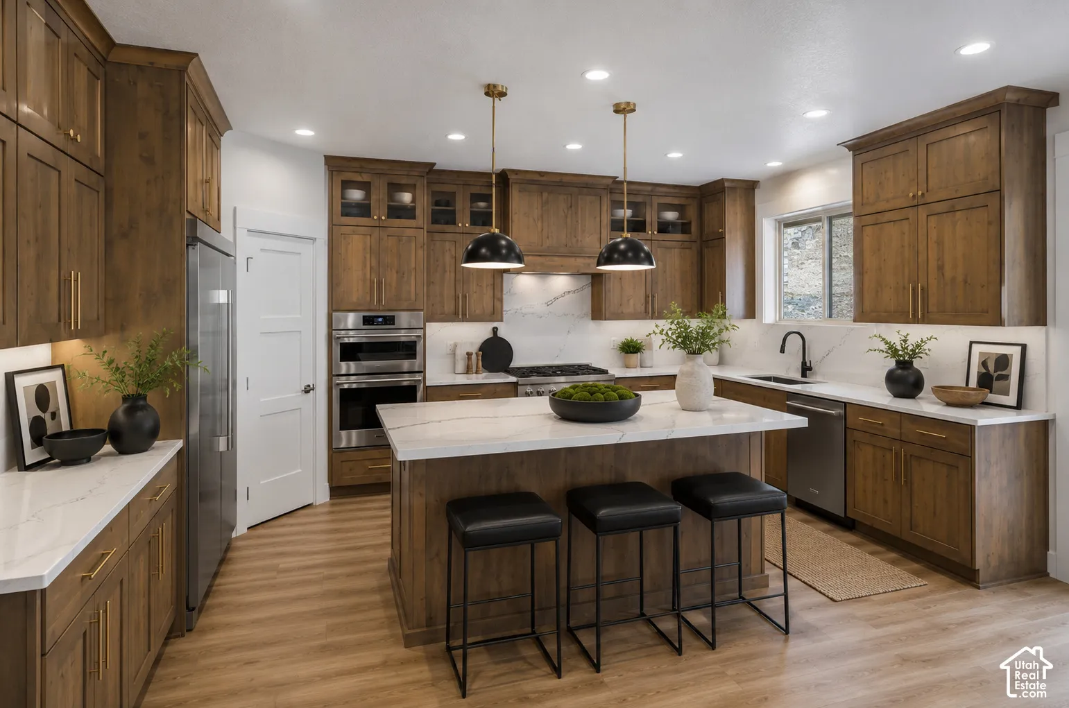 Modern kitchen featuring a large central island with seating, extensive wood cabinetry, light-toned countertops, stainless steel appliances, and recessed lighting