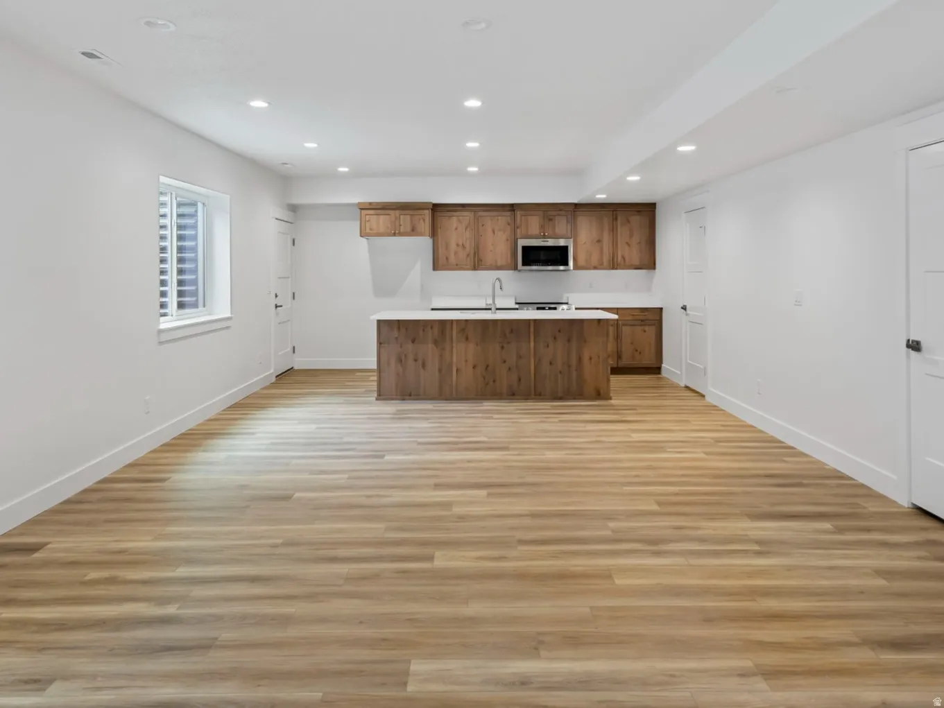 Spacious open-concept room featuring wood-finish flooring, recessed lighting, and a modern kitchen area