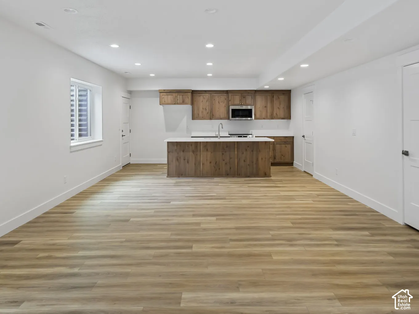 Spacious open-concept room featuring wood-finish flooring, recessed lighting, and a modern kitchen area