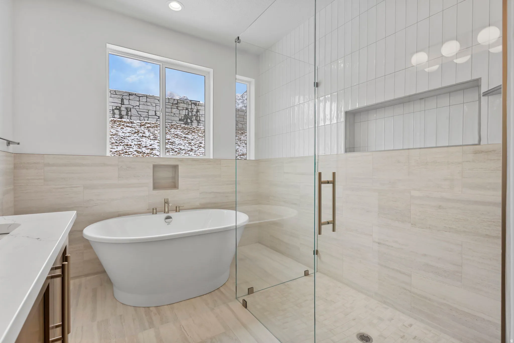 Spacious bathroom featuring a freestanding soaking tub with floor-mounted faucet, a glass-enclosed shower with subway tile surround, recessed lighting, and a white countertop vanity with dark-finish cabinetry