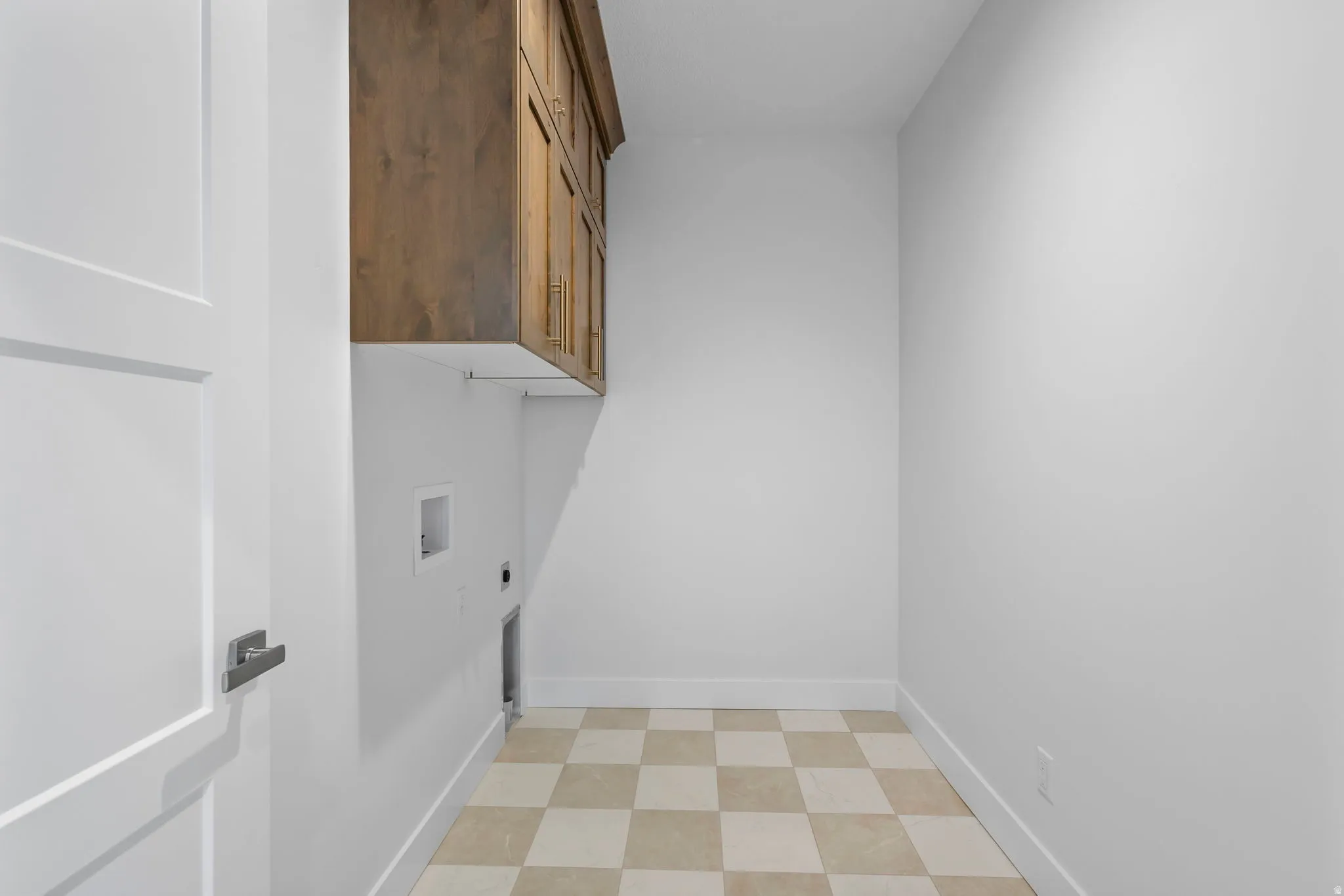 Utility room with checkerboard tile flooring, white walls, and built-in wood-finish cabinetry