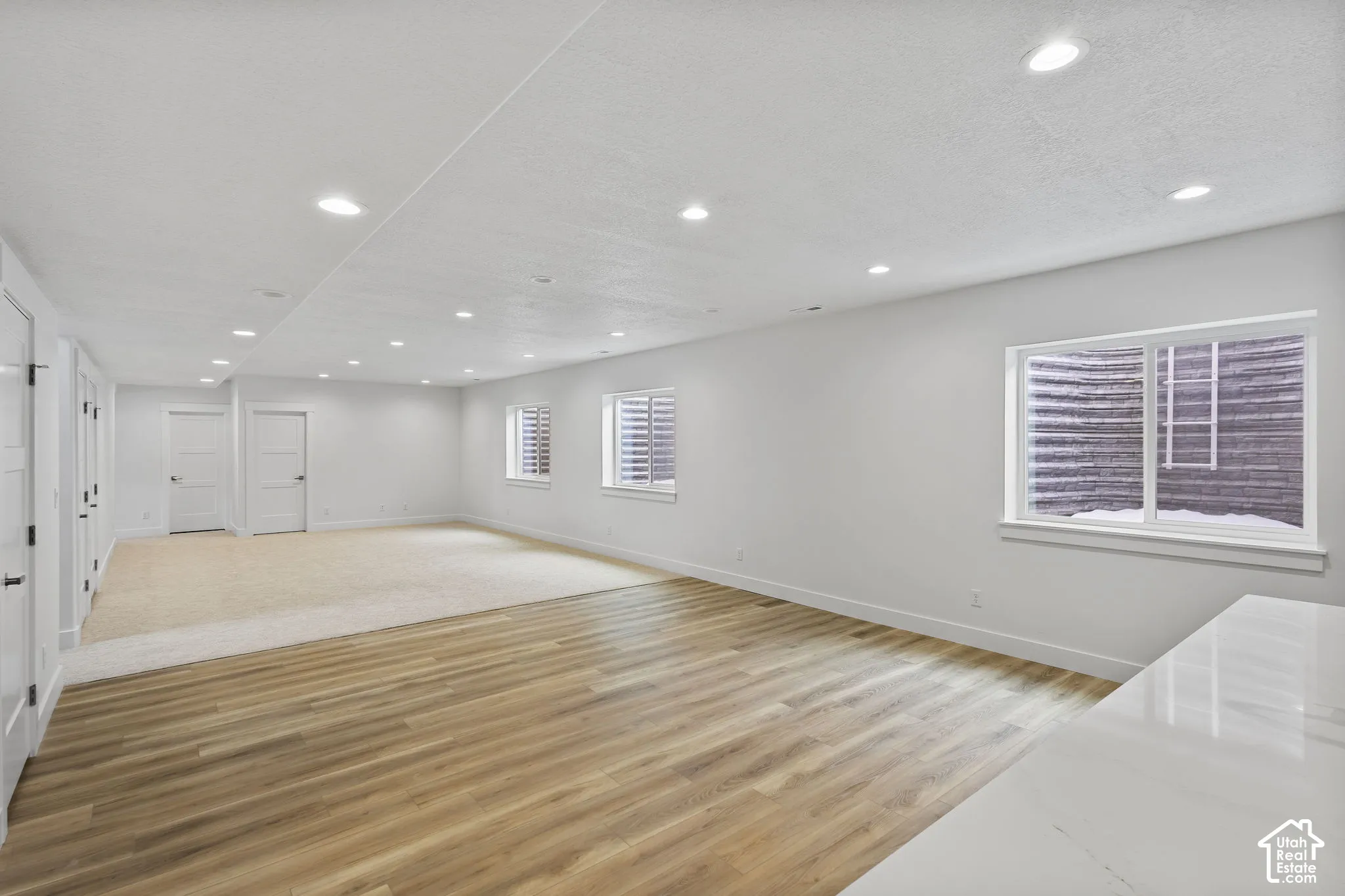 Spacious room featuring wood-finish flooring and neutral carpet, white walls, multiple recessed lights, and several white doors with black hardware