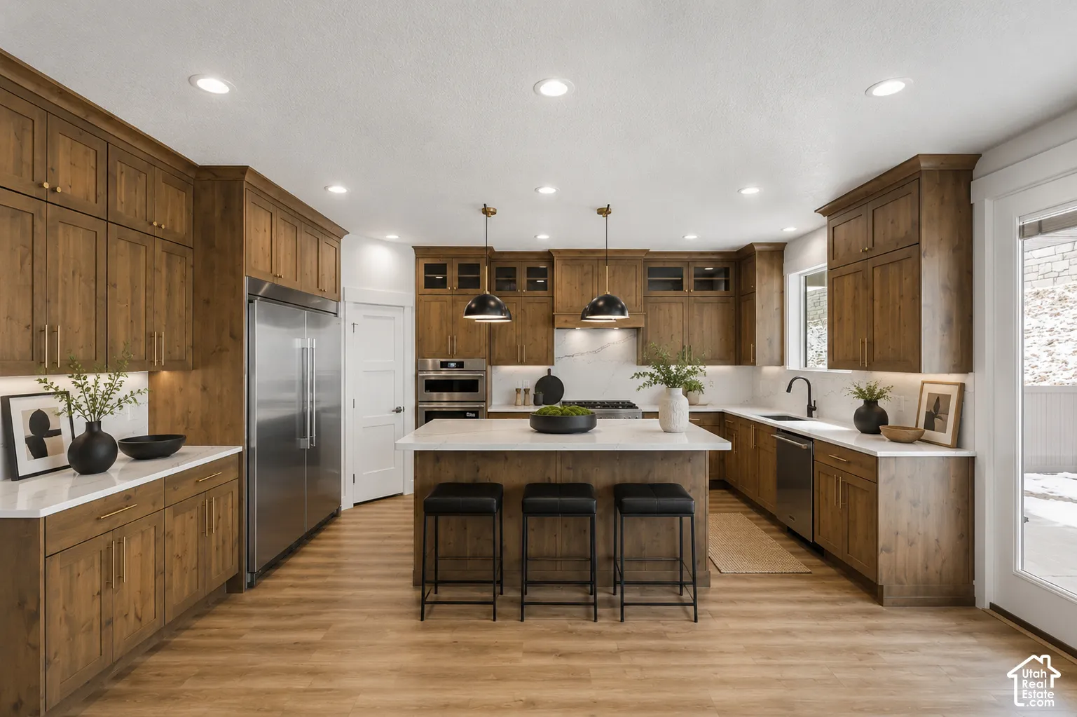 Gourmet kitchen featuring extensive wood cabinetry, stainless steel appliances, white countertops, recessed lighting, and a central island with pendant lighting