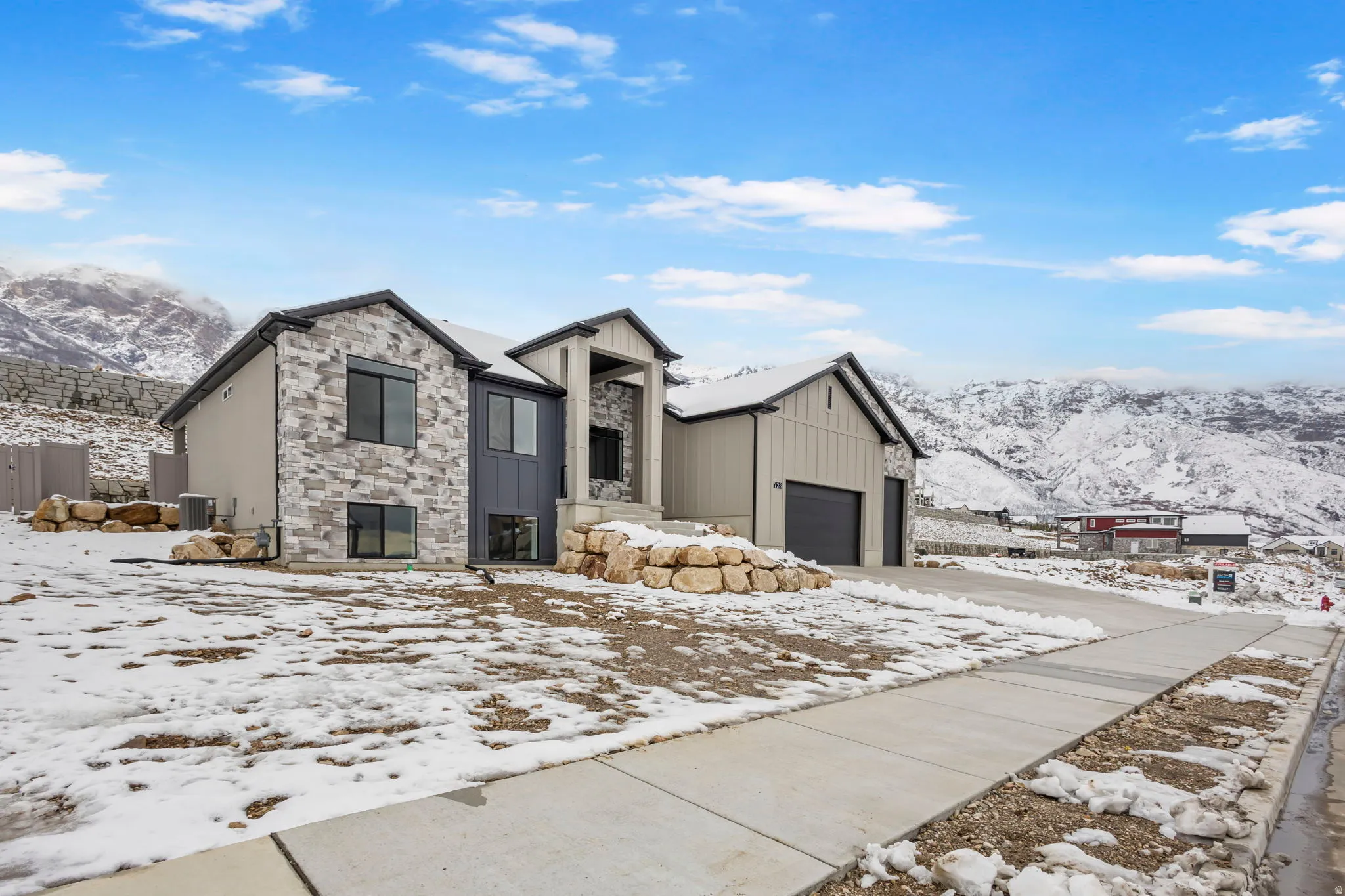 Modern architectural home featuring a multi-textured exterior, prominent stone accents, board and batten siding, dark-framed windows, and an integrated garage