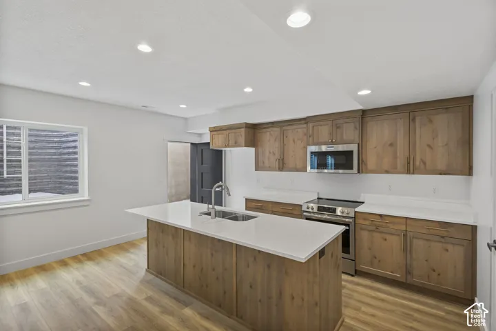 Bright kitchen featuring a central island with an undermount sink, light countertops, wood-finish flooring, and recessed lighting