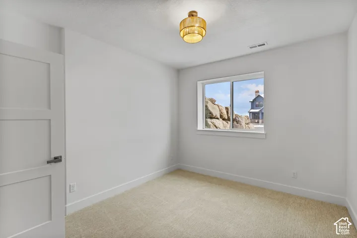 Neutral interior room featuring a light-colored carpet, white walls, and a contemporary light fixture