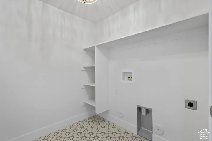 Laundry space featuring patterned floor tiles, built-in shelving, an overhead light fixture, and white baseboards
