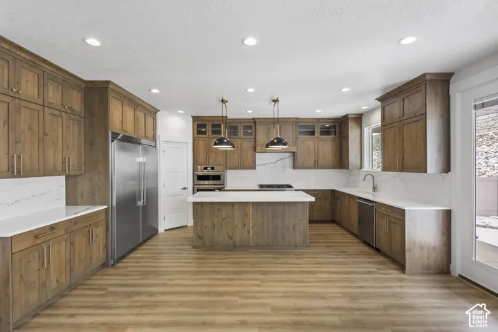 Spacious kitchen featuring extensive wood cabinetry, white countertops, a central island, recessed lighting, and stainless steel appliances