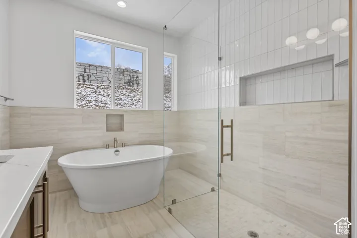 Spacious bathroom featuring a freestanding soaking tub with floor-mounted faucet, a glass-enclosed shower with subway tile surround, recessed lighting, and a white countertop vanity with dark-finish cabinetry
