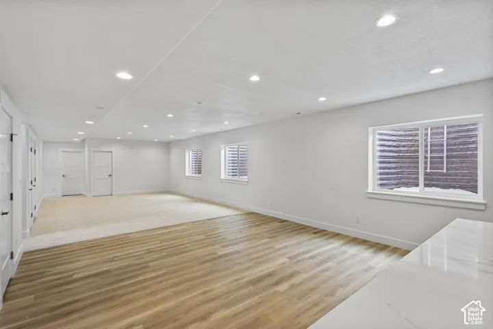 Spacious room featuring wood-finish flooring and neutral carpet, white walls, multiple recessed lights, and several white doors with black hardware