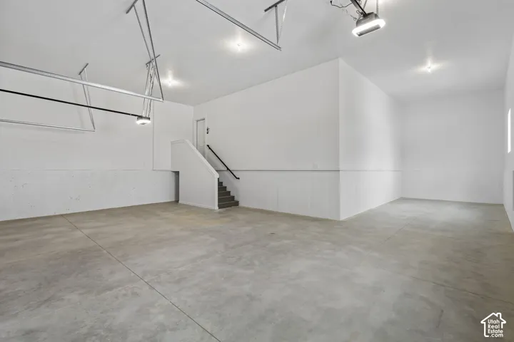 Spacious garage featuring a concrete floor, bright white walls, recessed lighting, and a built-in staircase with a handrail