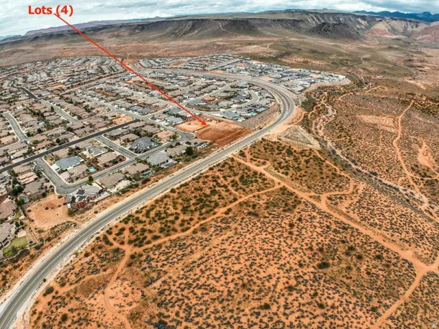 Four cleared land lots within a residential community, bordered by a paved road
