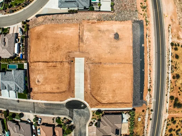 Expansive undeveloped lot featuring graded earth, bordered by a paved road and established residential properties