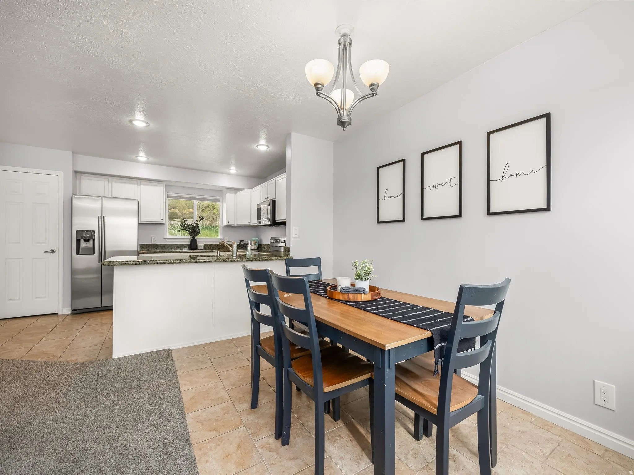 Open-concept kitchen and dining area featuring tile flooring, white cabinetry, stainless steel appliances, and recessed lighting