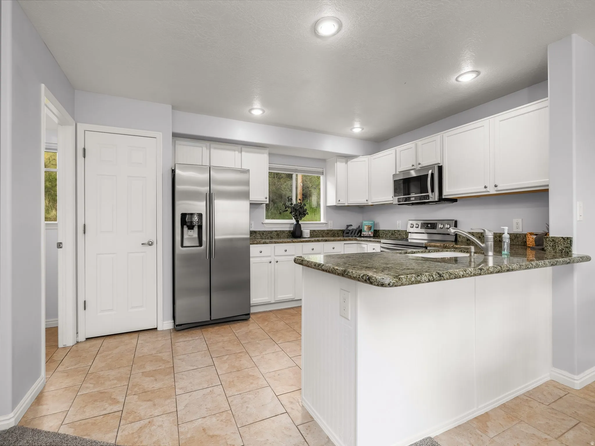Kitchen featuring white cabinetry, stainless steel appliances, recessed lighting, a built-in kitchen island with stone countertops, and tile flooring