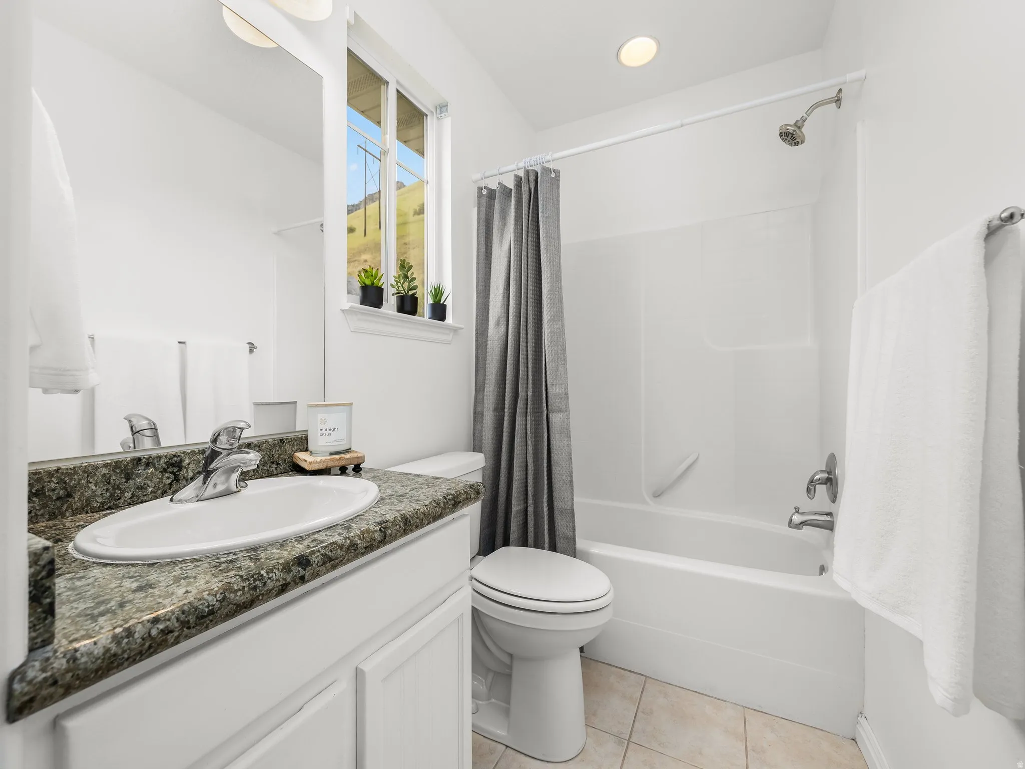 Bathroom featuring a white vanity with a speckled countertop and integrated sink, a white toilet, a white bathtub with an overhead shower, and neutral tile flooring
