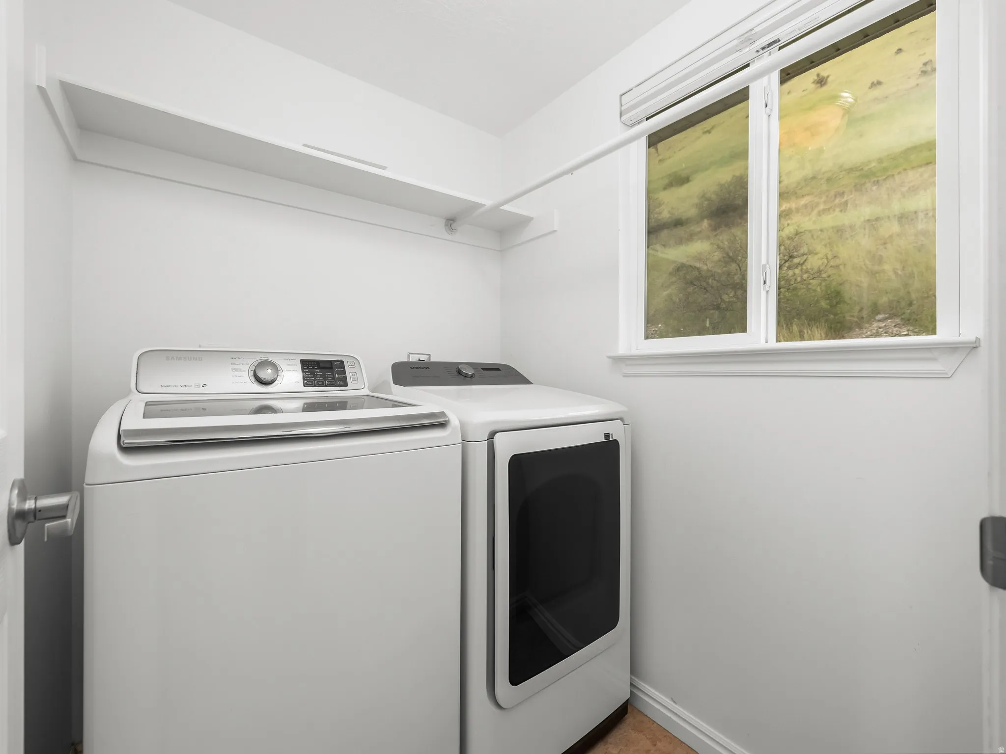 Dedicated laundry room featuring a large window, integrated shelving, and a hanging rod