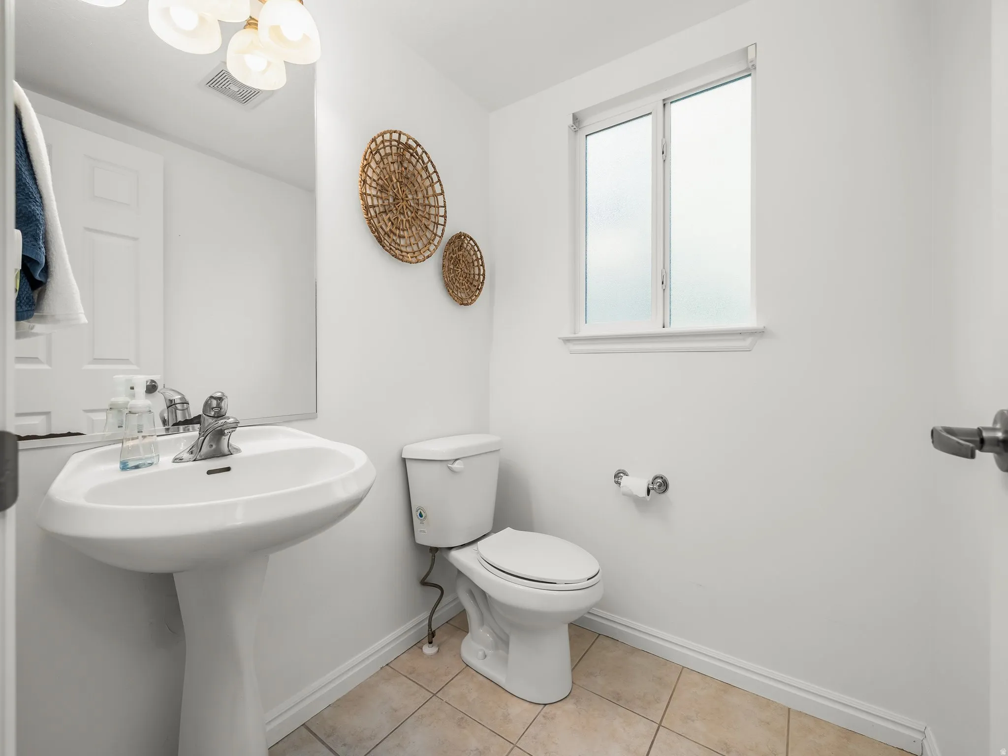 Pedestal sink with chrome faucet, light tile flooring, and a window with white trim