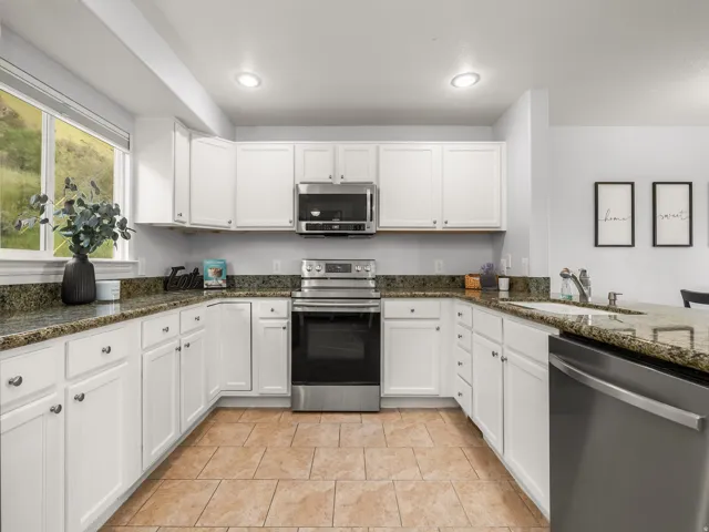 U-shaped kitchen featuring white cabinetry, granite countertops, stainless steel appliances, and tile flooring