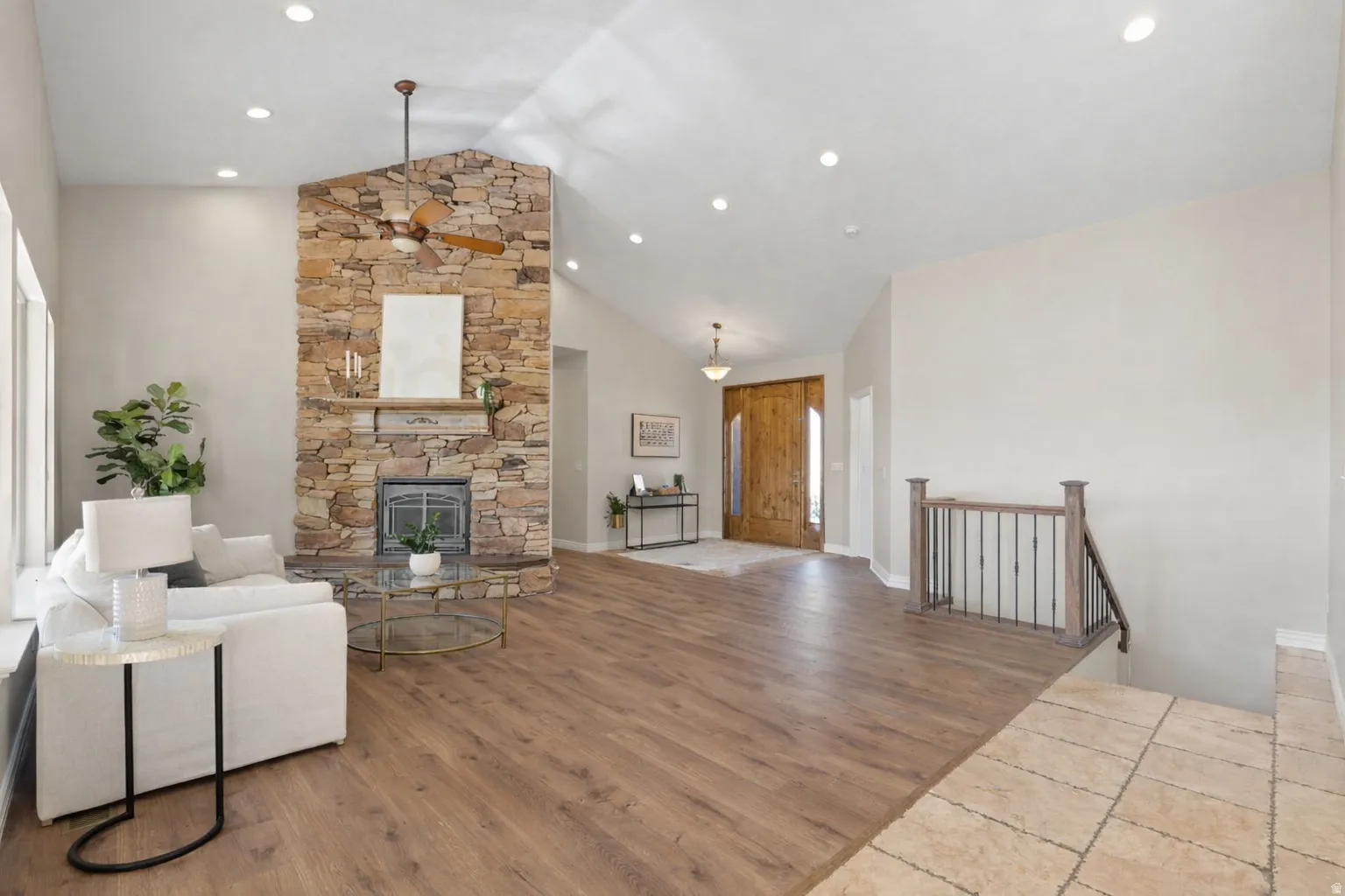 Vaulted ceiling living space with a floor-to-ceiling stone fireplace, wood-finish flooring, recessed lighting, a ceiling fan, and a wood entry door