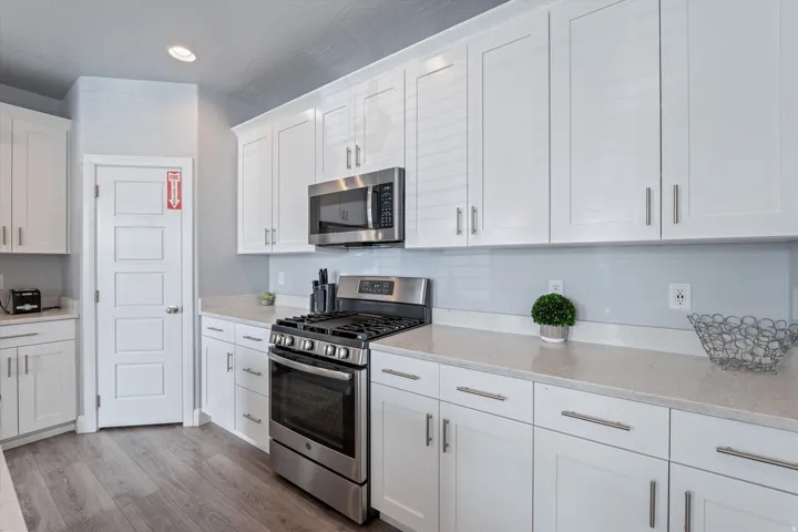 Kitchen featuring white shaker cabinetry, stainless steel appliances, stone-finish countertops, subway tile backsplash, and wood-finish flooring