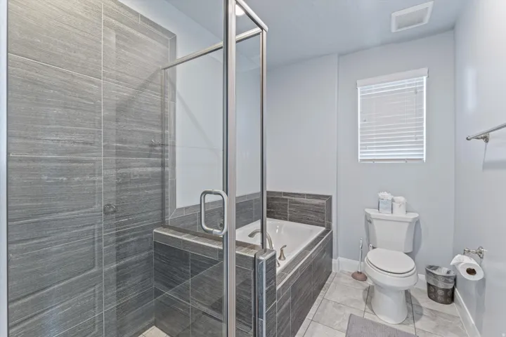 Bathroom featuring a glass-enclosed shower with gray tiled walls, a built-in tub with matching gray tile surround, and light gray floor tiles