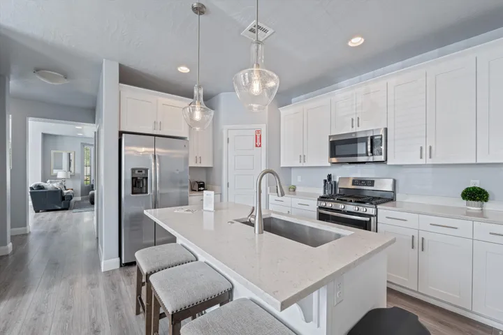 Modern kitchen featuring an island with a built-in sink, stainless steel appliances, white cabinetry, light-colored countertops, and wood-finish flooring