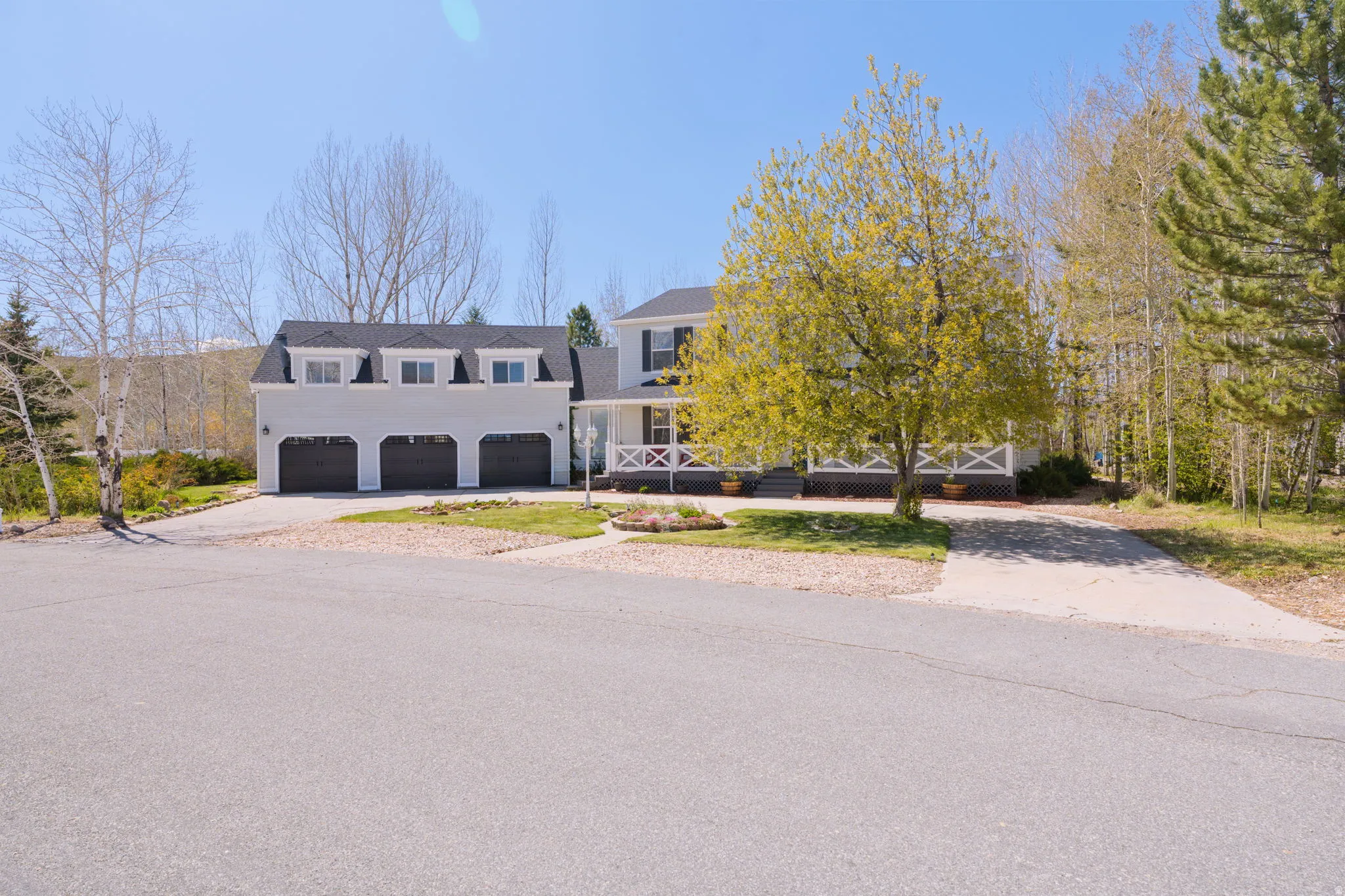 Traditional-style home featuring a three-car garage with dormer windows, a covered front porch with white railing, and a gabled roofline
