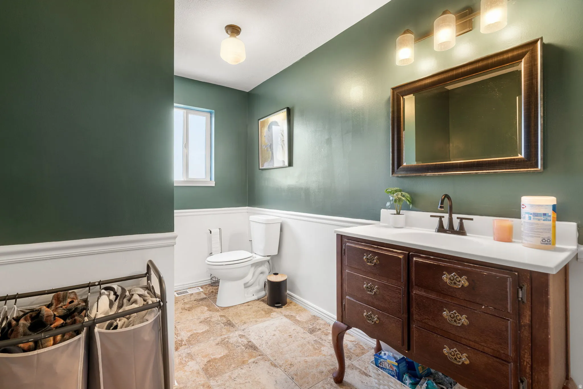 Bathroom featuring a dark wood vanity with a white countertop and integrated sink, bronze-finish faucet, and a large framed mirror with three-light fixture
