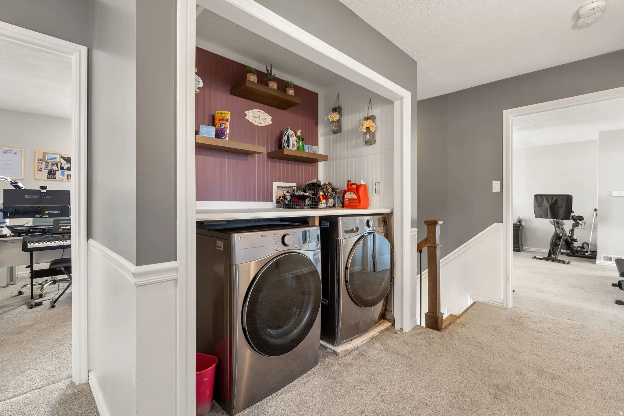 Dedicated laundry alcove featuring stacked front-loading appliances, beadboard paneling, and two floating wood-finish shelves