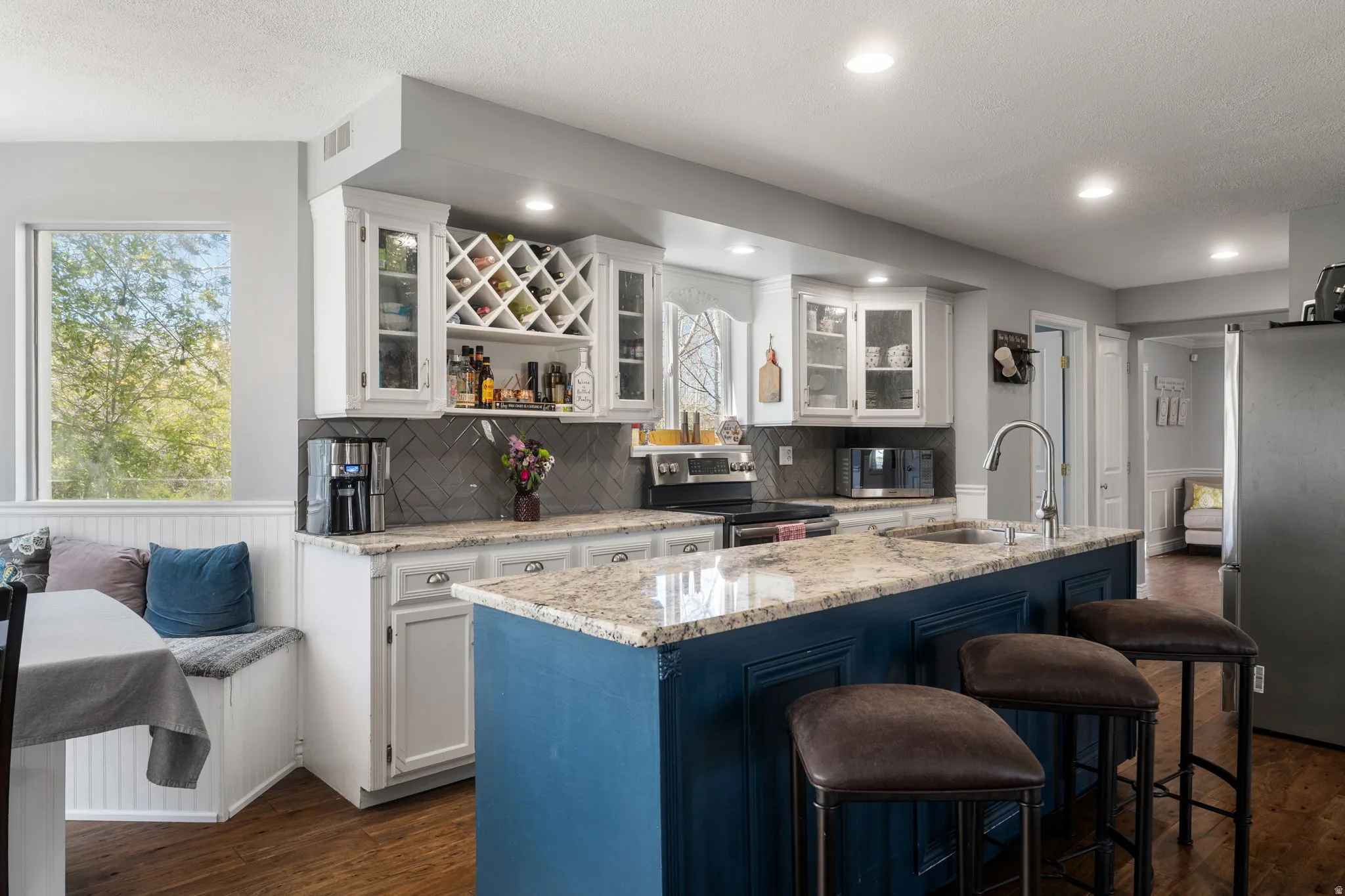 Kitchen featuring a central island with a granite-style countertop, white cabinetry with glass inserts, a built-in wine rack, tile backsplash, and recessed lighting