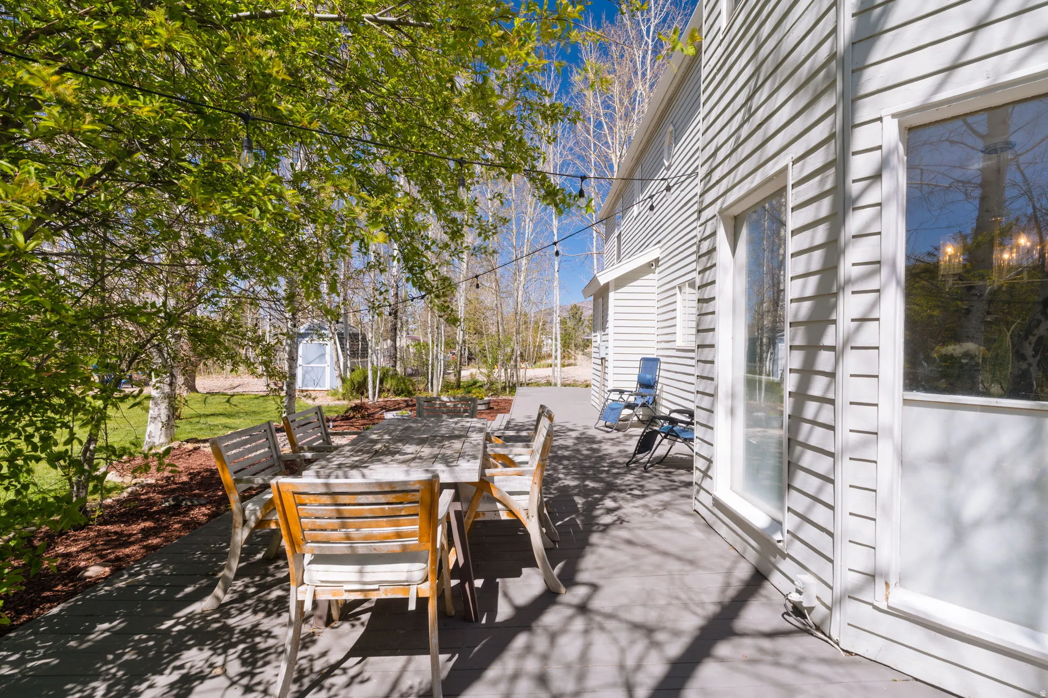 Expansive outdoor patio featuring a gray deck surface, string lighting, and mature trees providing natural shade