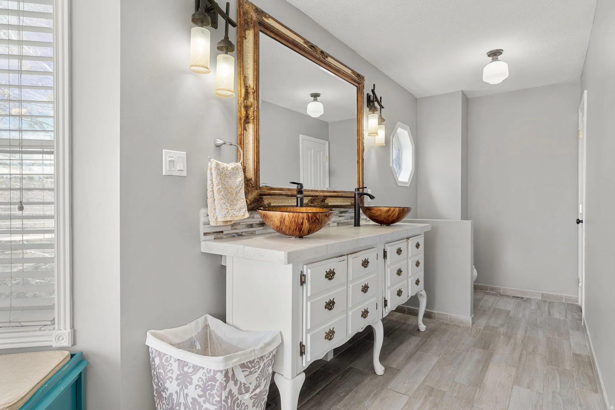 Bathroom featuring a double vanity with vessel sinks, ornate mirror, and wood-finish flooring