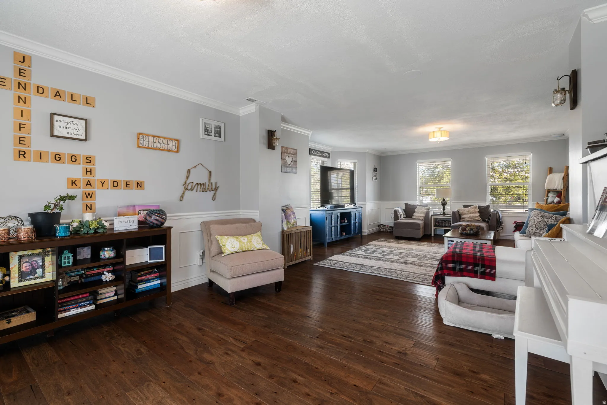 Spacious living area featuring wood-finish flooring, light gray wall paint, white crown molding, and wainscoting