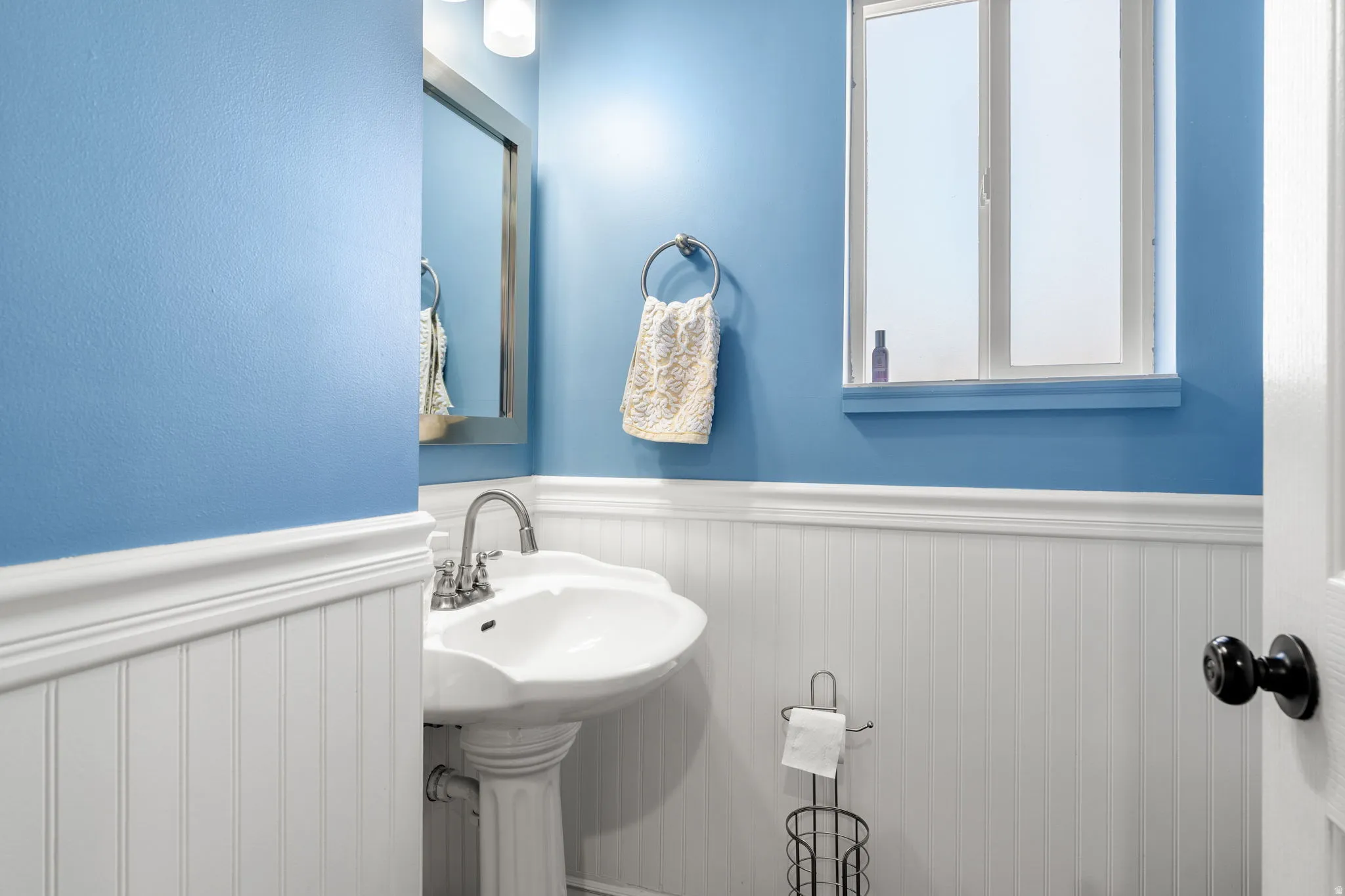 Pedestal sink with chrome faucet, complemented by white wainscoting and blue walls
