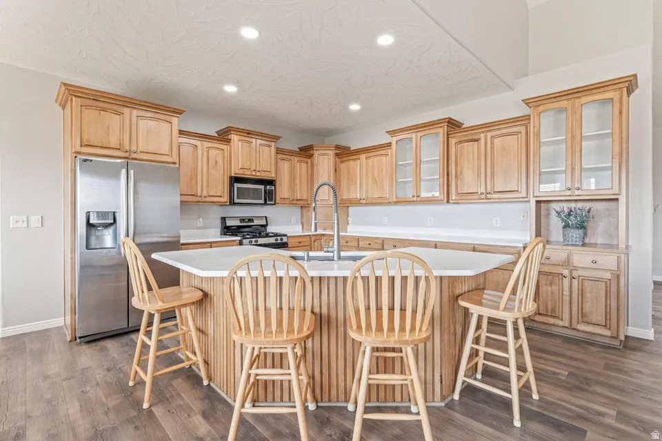Kitchen featuring wood-finish cabinetry, stainless steel appliances, a center island with countertop seating, white countertops, and wood-finish flooring