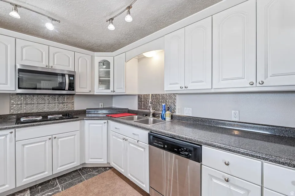 Kitchen featuring white cabinetry, dark speckled countertops, stainless steel appliances, and a textured backsplash