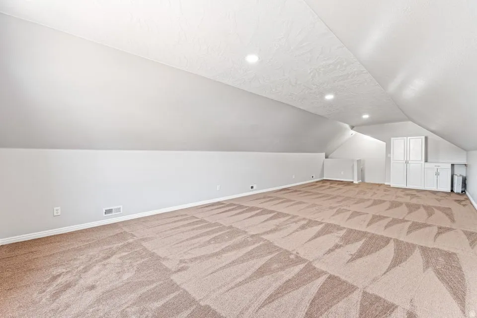 Expansive carpeted room featuring a textured ceiling with recessed lighting