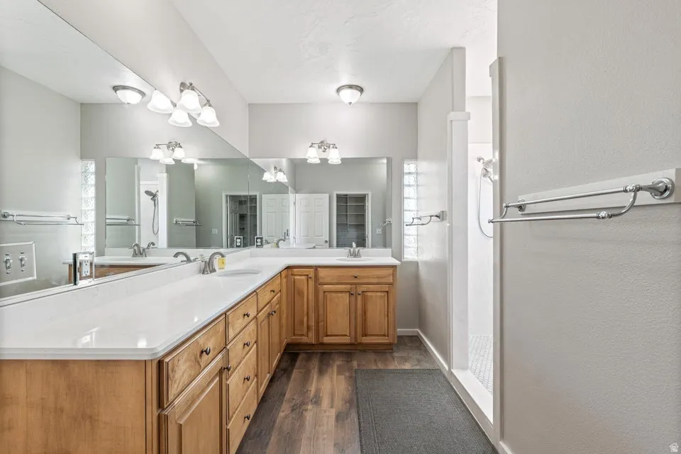 Expansive bathroom featuring dual wood-finish vanities with white countertops, large wall-mounted mirrors, and wood-finish flooring