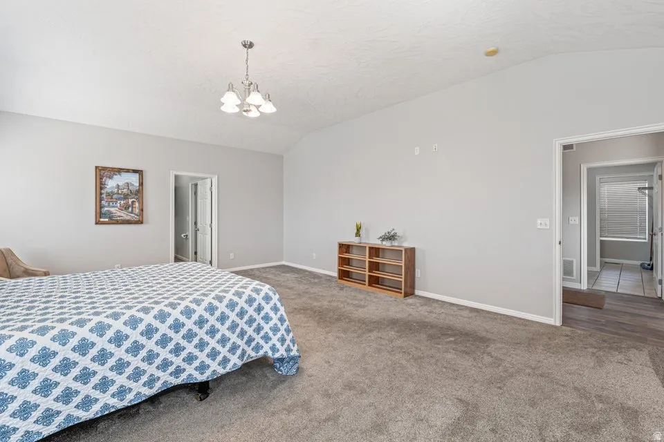 Spacious bedroom featuring vaulted ceilings, light gray wall paint, and gray carpeting