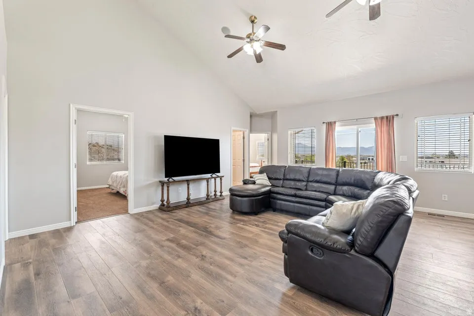 Spacious living area featuring vaulted ceilings, wood-finish flooring, multiple windows with horizontal blinds, and two ceiling fans