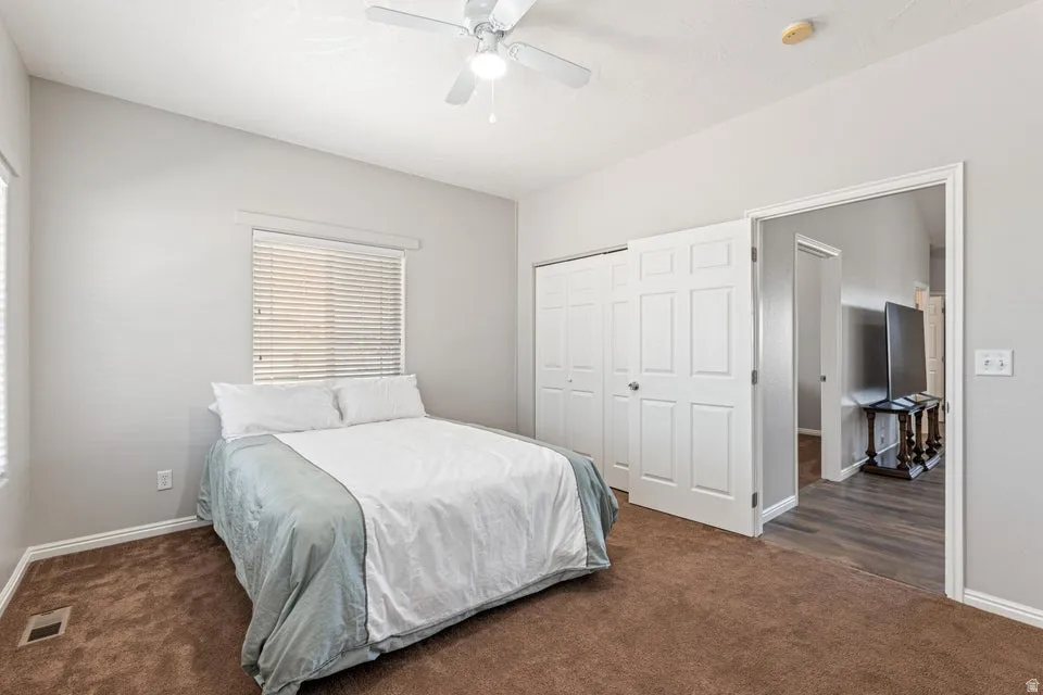 Carpeted bedroom with vaulted ceilings, a ceiling fan, and two windows with blinds