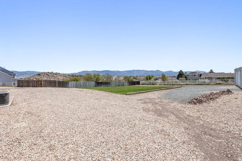 Expansive gravel area with a green lawn portion and partial wood fencing