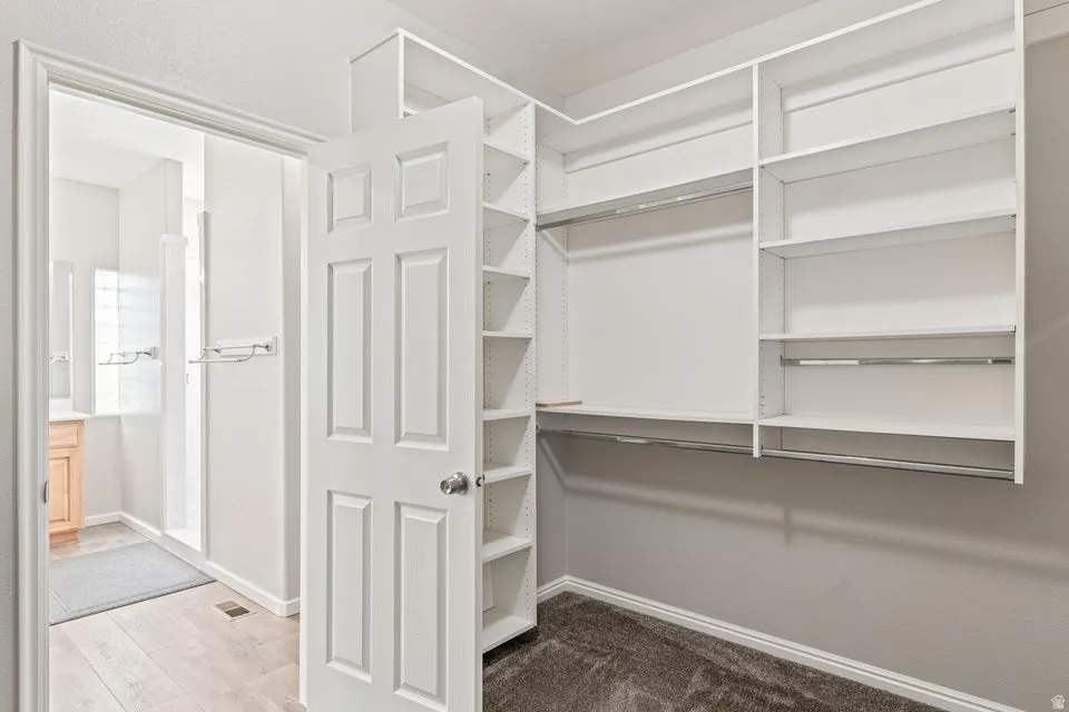 Walk-in closet featuring built-in shelving, multiple hanging rods, and dark carpeting