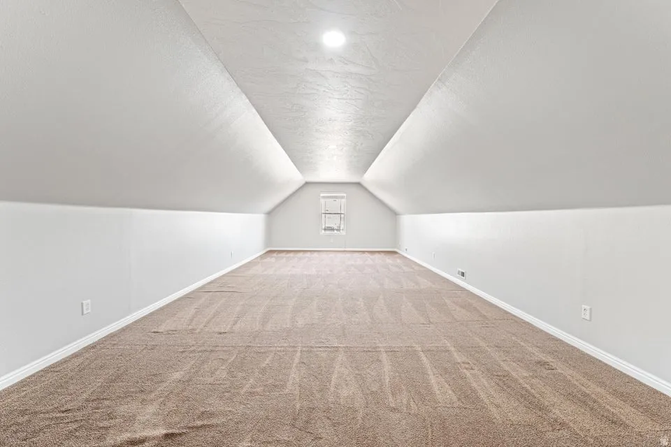 Expansive carpeted room featuring a vaulted ceiling with recessed lighting, white baseboards, and a rear window