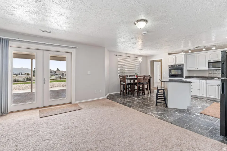 Open-concept living space featuring a carpeted area, French doors leading to an exterior patio, and a dining area with a chandelier